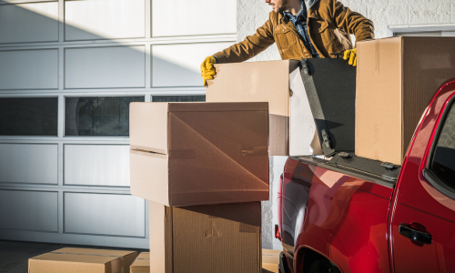 An individual putting cardboard boxes in the bed of a pickup truck.