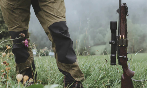 A hunter standing in a field next to a long rifle.