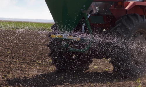 Fertilizer being spread out of a tractor onto a crop field.