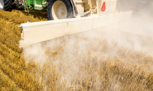 Fertilizer being sprayed out of a tractor onto a crop field.